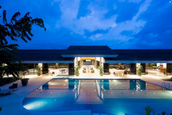 A luxurious building with a large illuminated pool at night, surrounded by seating areas and a clear blue sky overhead.