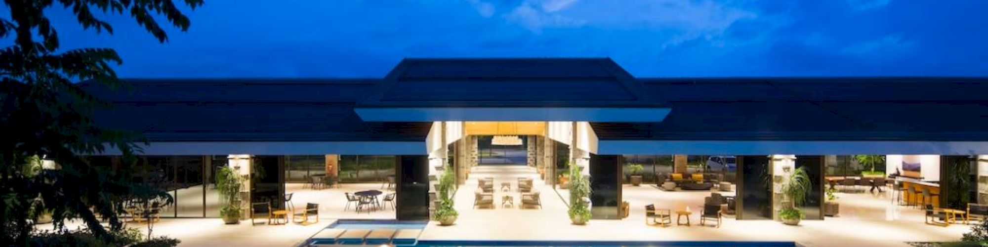 A luxurious modern building with a large illuminated pool in the foreground, surrounded by a serene evening setting.