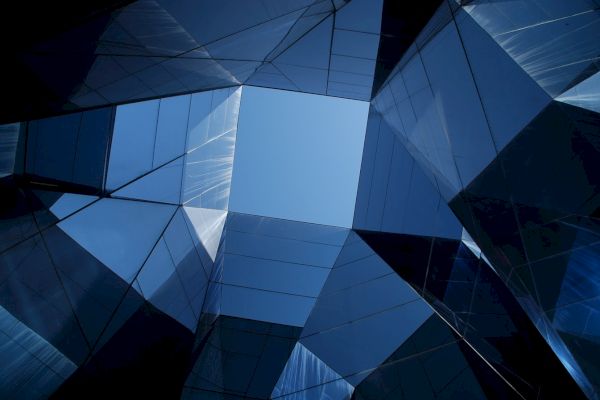 Looking up at a geometric glass building, creating a symmetrical pattern against the clear blue sky.