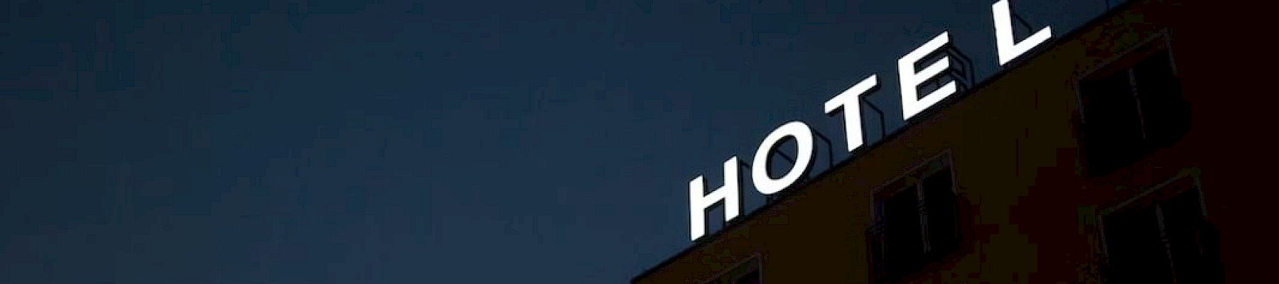 A building at night with a lit "HOTEL" sign missing an "L" against a dark sky.