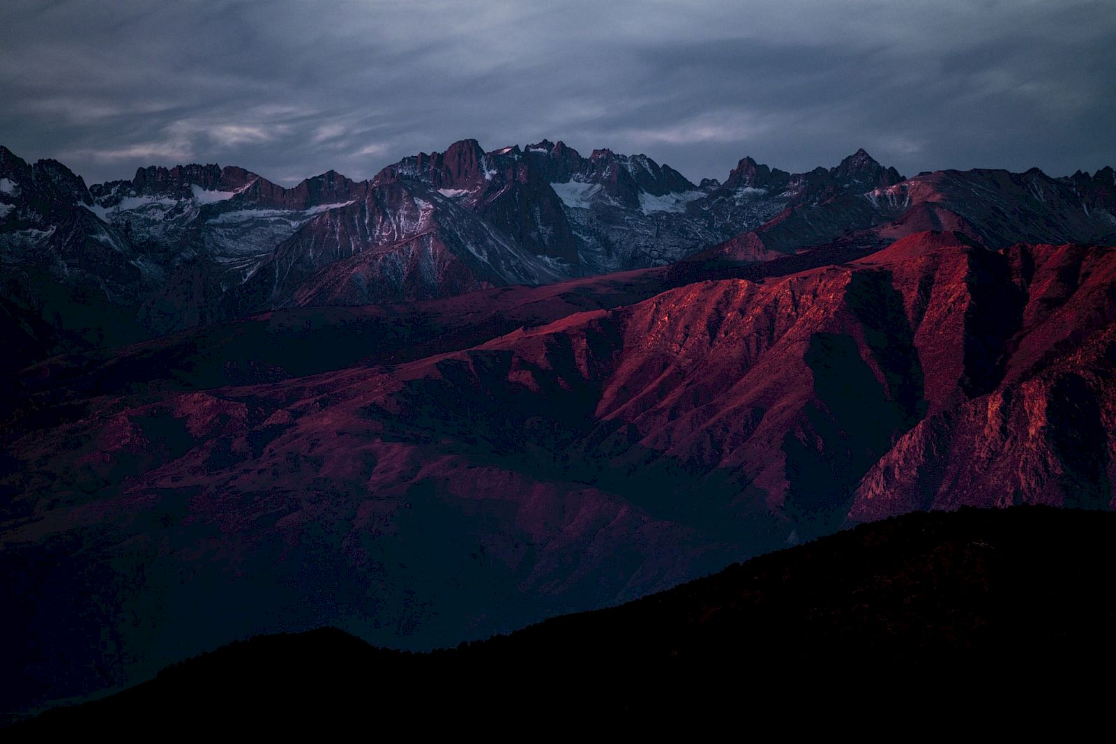 A mountain range with dramatic lighting and cloudy sky, creating a striking contrast.