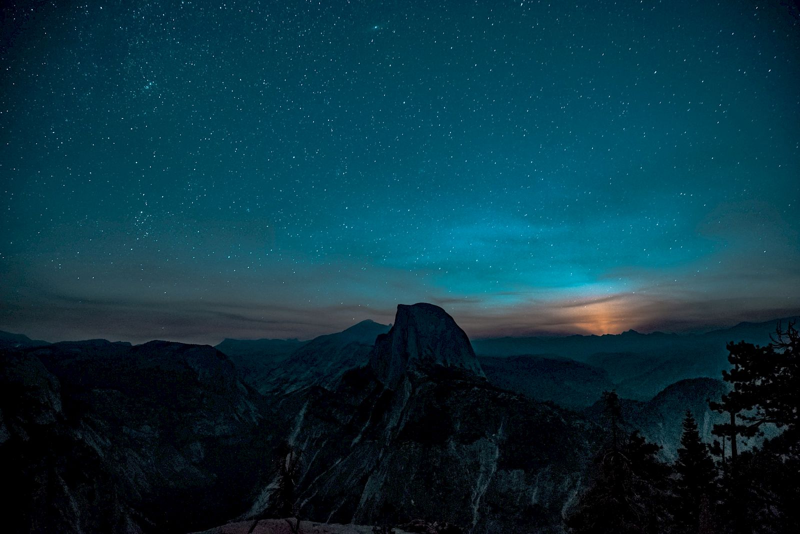 A starry night sky over a mountainous landscape with a glowing horizon, likely at dusk or dawn, creating a serene and majestic scene.