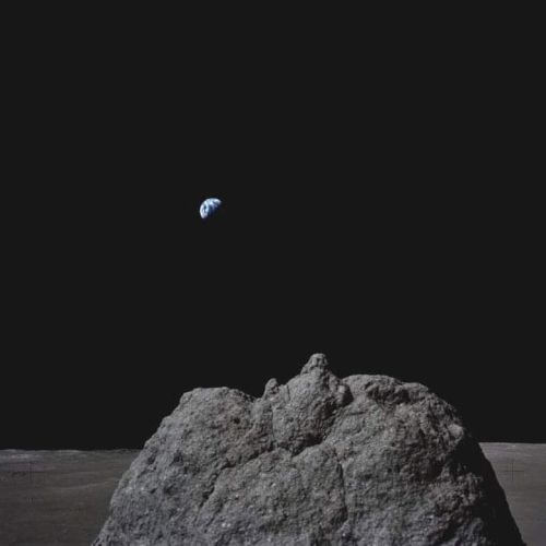 A view from the moon showing a large rock in the foreground and Earth visible in the distant background against a black sky.
