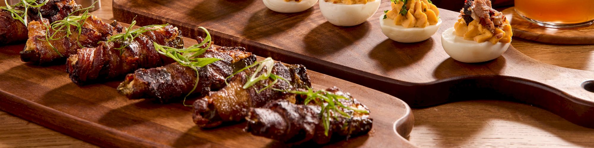 A spread of appetizers including deviled eggs, wings, nachos, chips, and various drinks on wooden serving boards.
