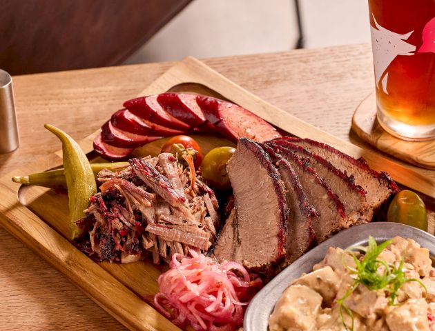 A BBQ platter with brisket, sausage, pickles, onions, potato salad, and a beer.