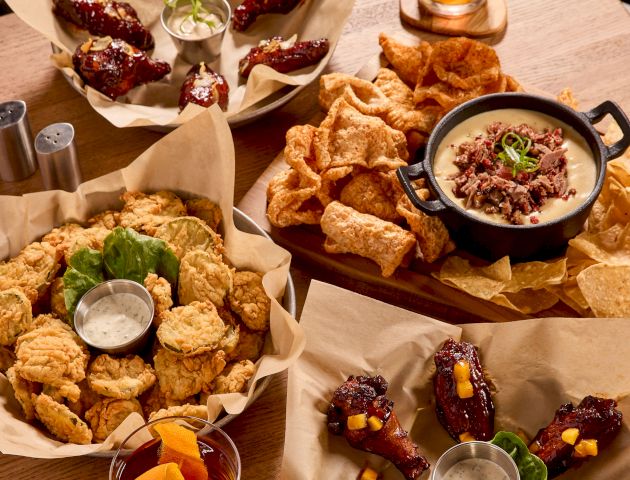 A table with various appetizers: fried foods, wings, chips with dip, and two glasses of drinks. Perfect for sharing and enjoying.