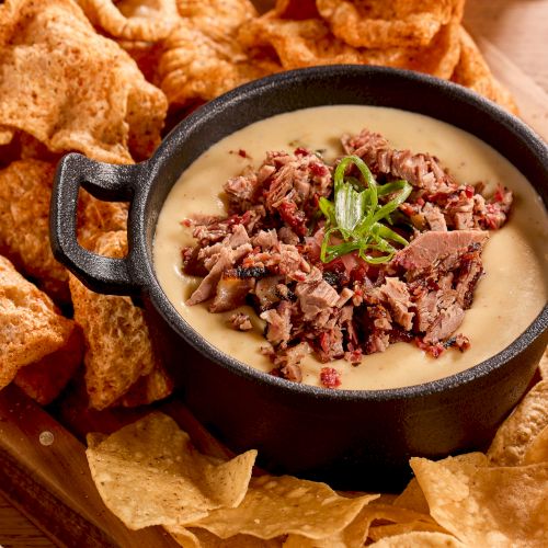 Creamy cheese dip topped with chopped beef, surrounded by crispy tortilla chips in a black serving dish.
