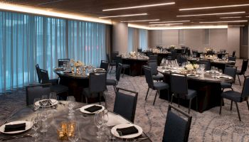 The image shows an elegant banquet hall with round tables set for an event, featuring black chairs and dim lighting.