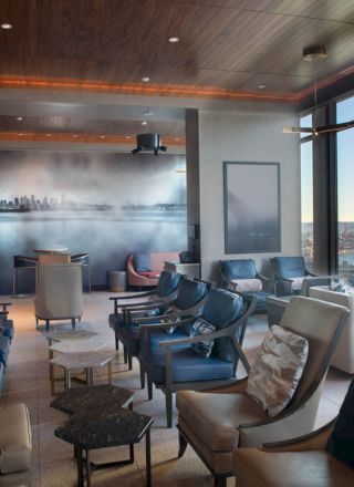 A modern lounge with leather chairs, a mural of a city skyline, and large windows offering a view of the water and a distant Ferris wheel.