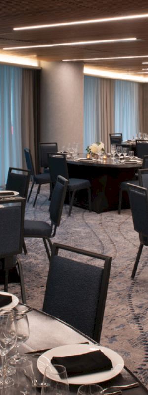 A banquet hall with round tables is set for an event, featuring black chairs, elegant table settings, and softly lit ambiance.