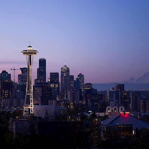 Seattle skyline at dusk with the Space Needle and Mount Rainier in the background, under a colorful sky.