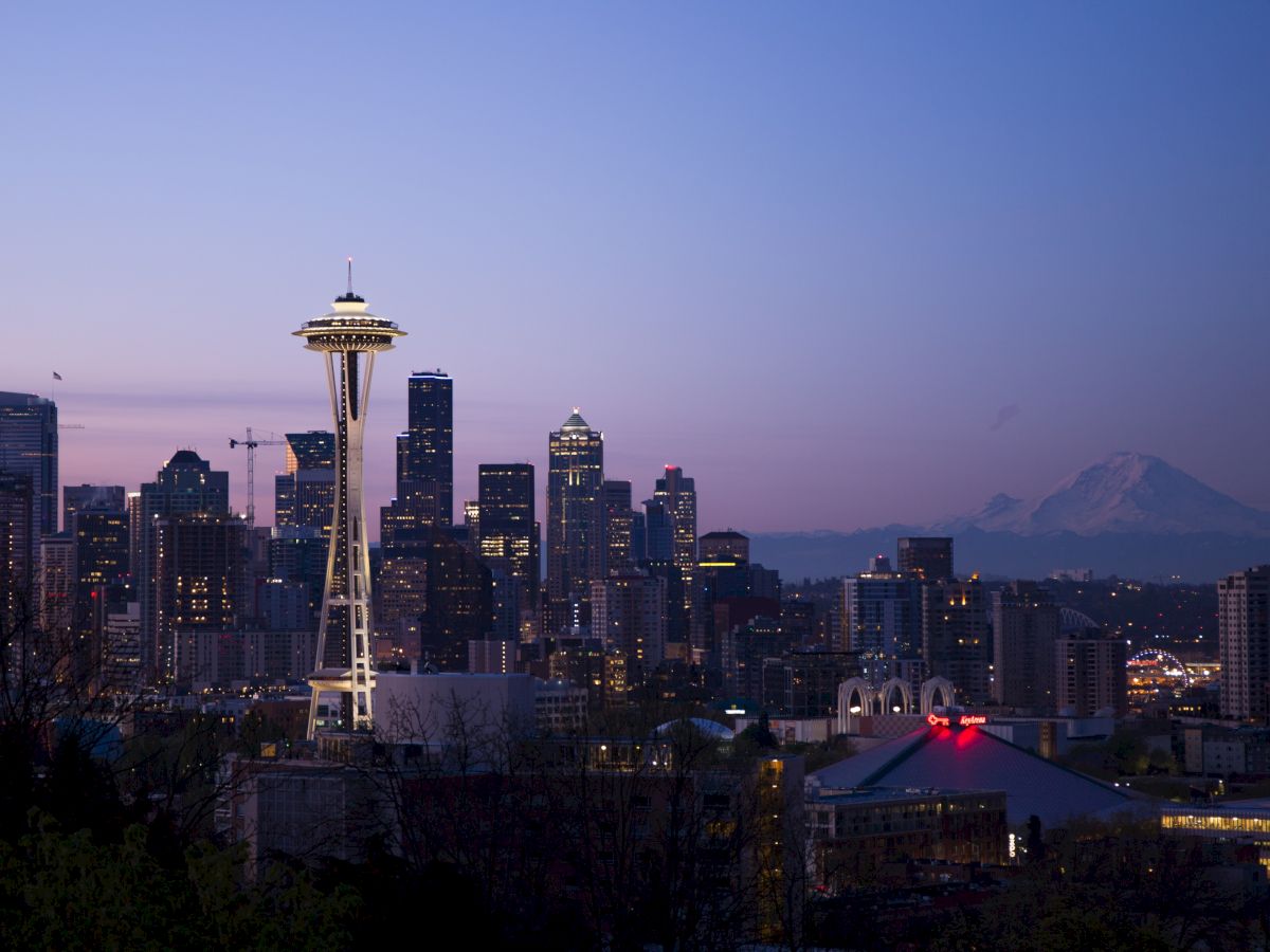 Seattle skyline at dusk with the Space Needle and Mount Rainier in the background, capturing city lights and twilight hues.