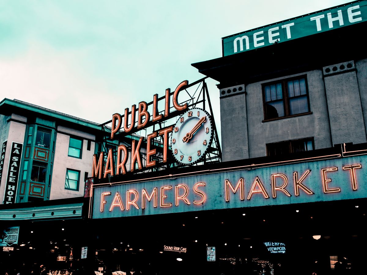 The image shows the iconic entrance of Public Market and Farmers Market with neon signs and a clock, in an urban setting.