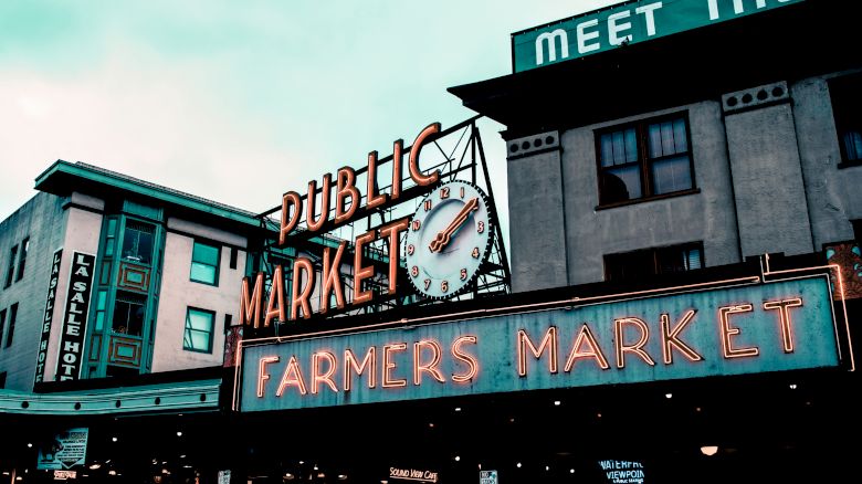 The image shows the iconic entrance of Public Market and Farmers Market with neon signs and a clock, in an urban setting.